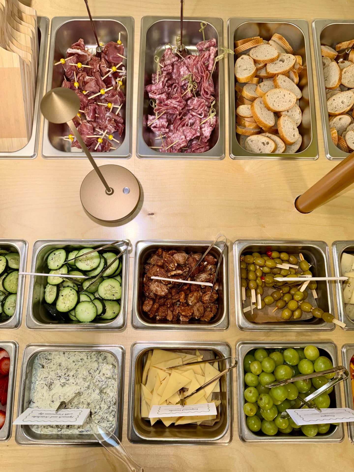 Overhead view of the cart's trays of prosciutto, salami, baguette, cucumbers, olives and grapes