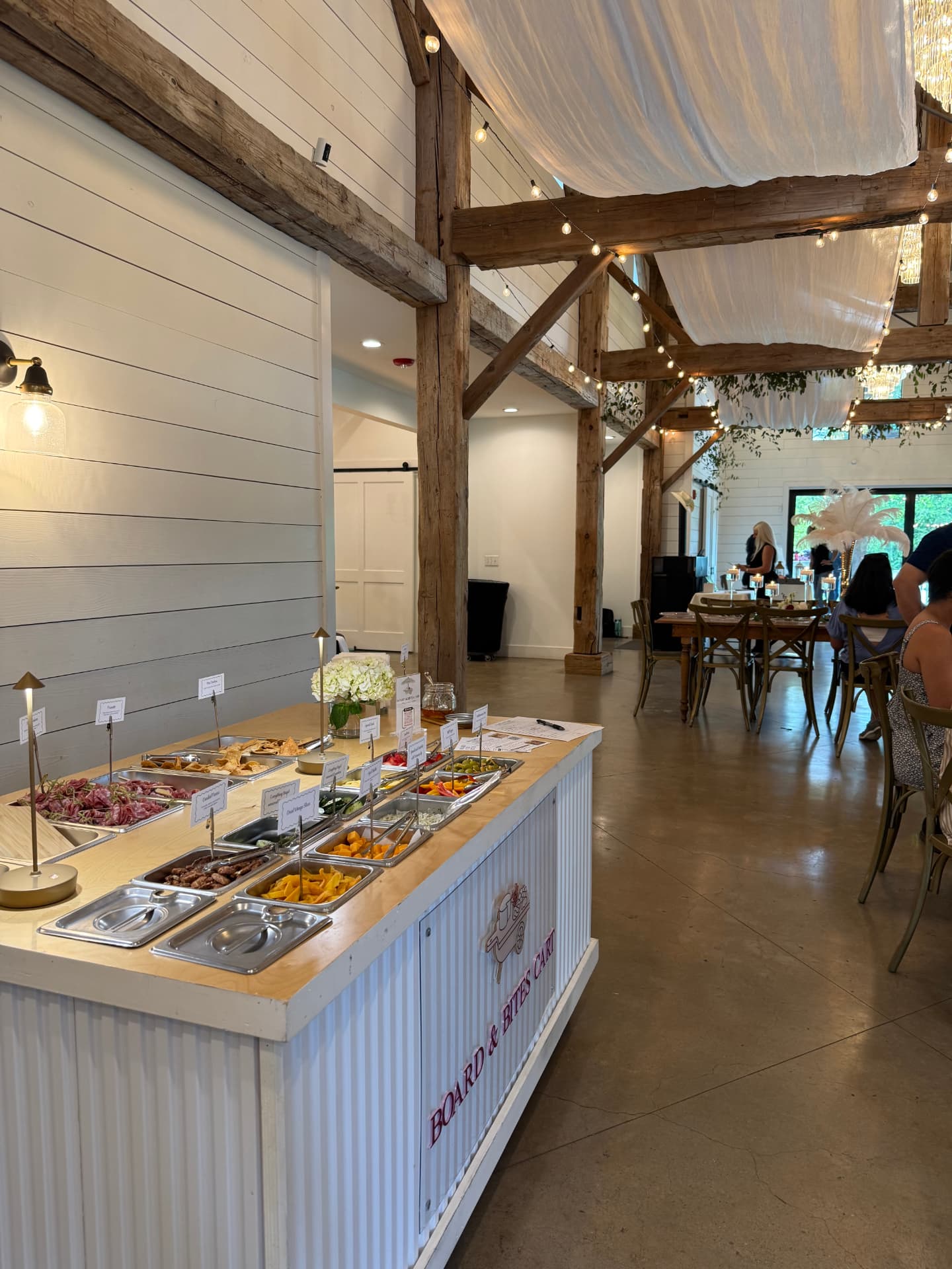 The branded Board & Bites Cart inside a white barn wedding venue