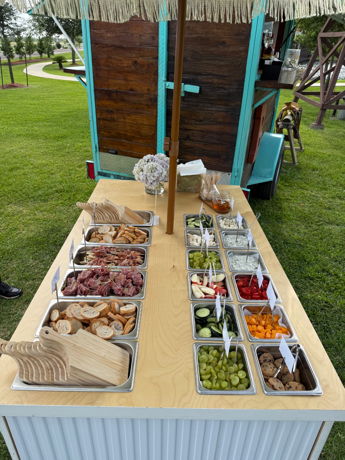 Full grazing table of meats, cheeses, breads and fruit beside the cart on a lawn