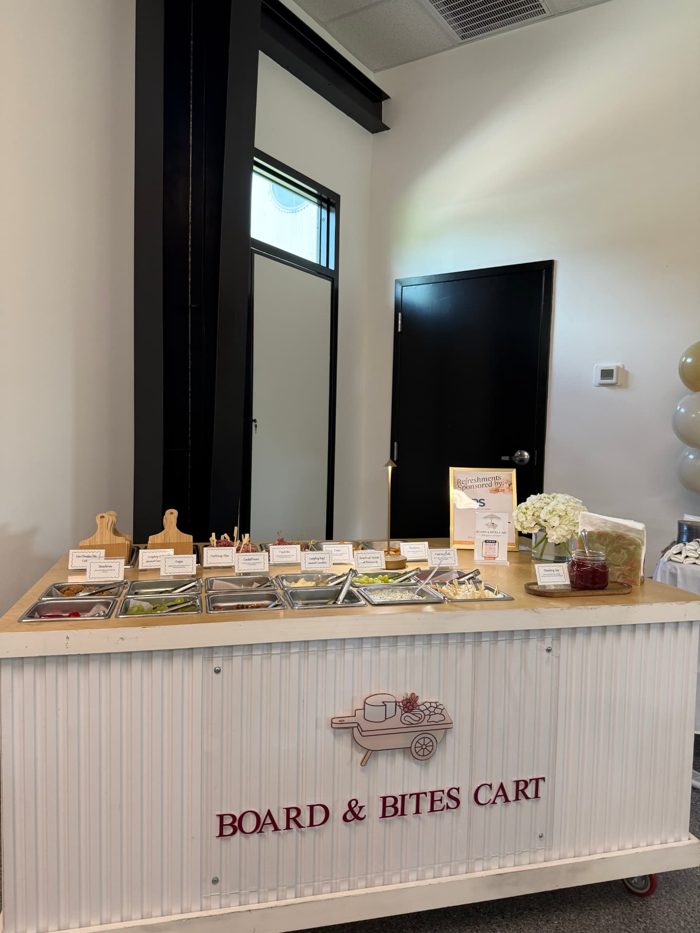 The charcuterie cart set up indoors with grazing trays, florals and labeled tins