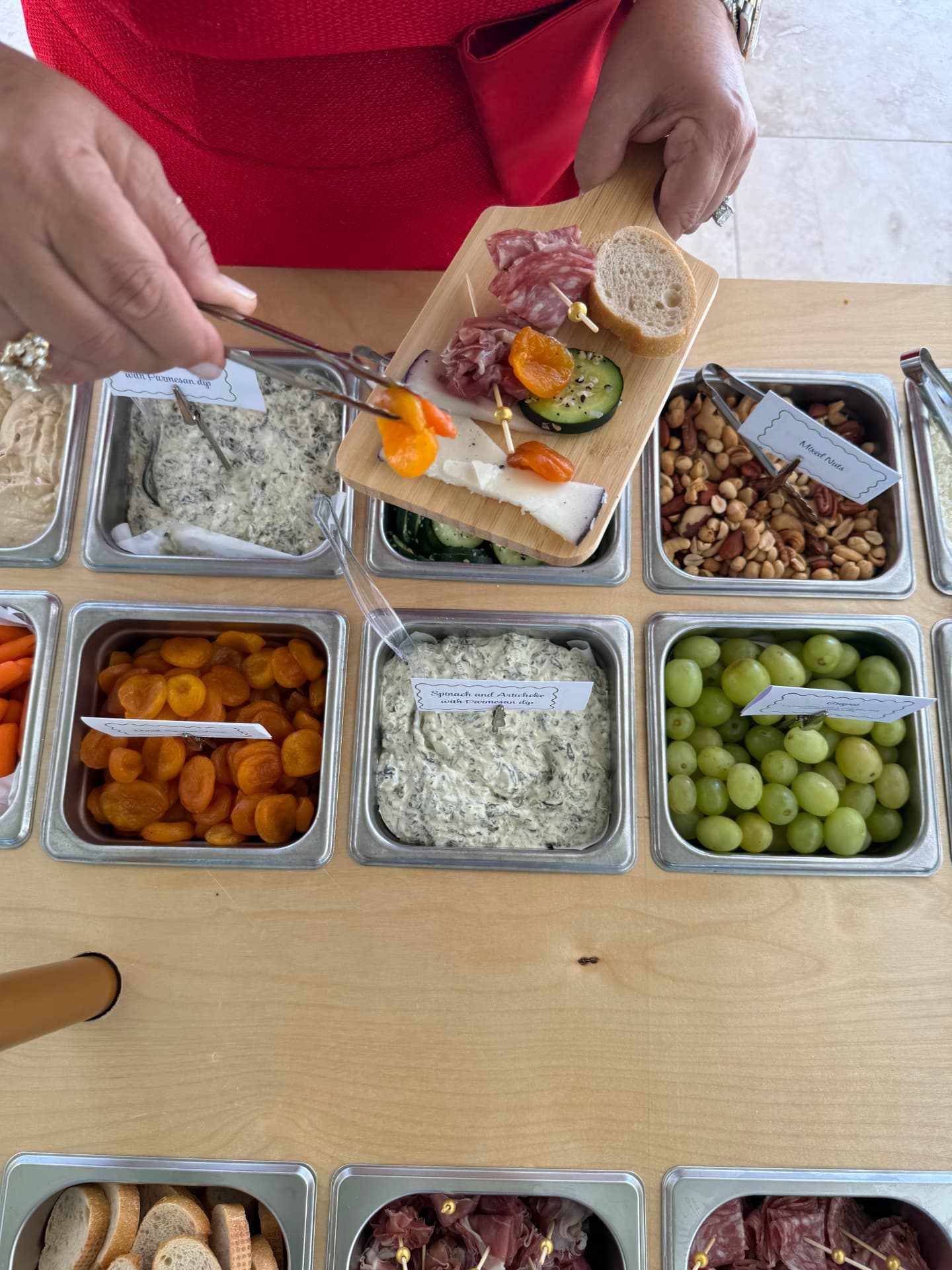A guest building a board with dried apricots, cheese and spinach artichoke dip at the cart